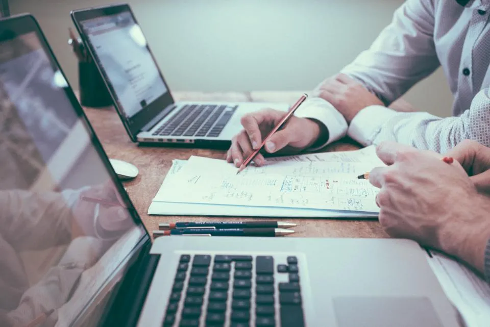 Two people auditing business listings side by side on laptops
